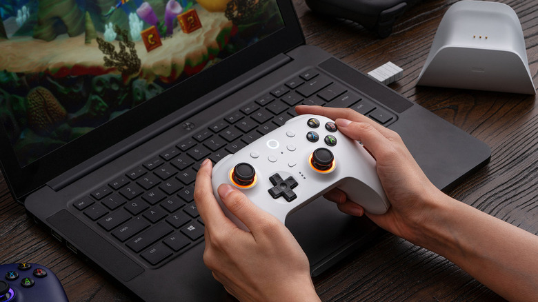 A person playing the 8BitDo Ultimate 2 with a laptop