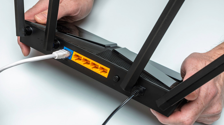 person holding a black router with four antennas with a LAN and power cable connected to it