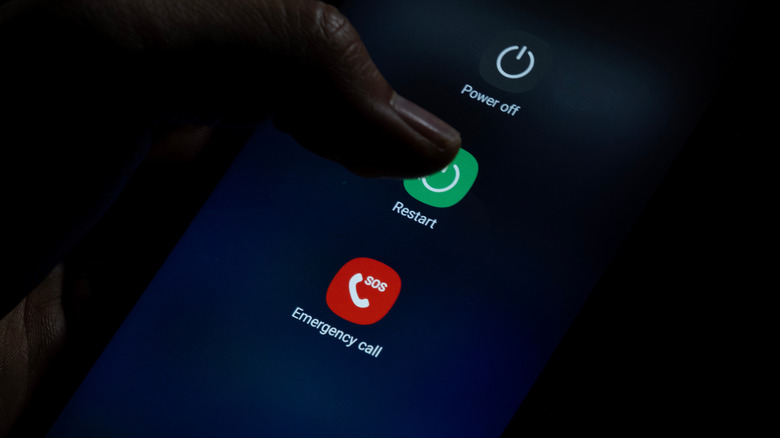 person tapping the restart option in the power menu of a smartphone