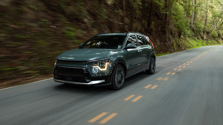 A green 2026 Kia Niro parked in field near a tree and a grassy hill