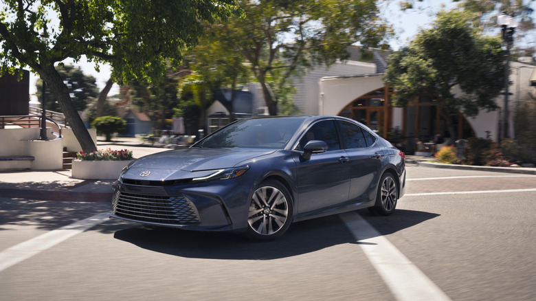 A light blue 2026 Toyota Camry on the road with trees and buildings behind it