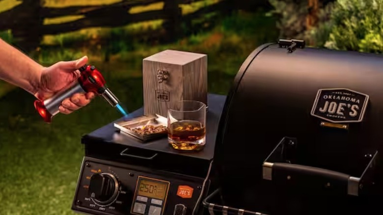 Person using torch with Oklahoma Joe's smoking box