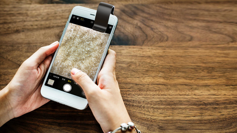 A person holding a smartphone with a clip-on microscope lens, displaying a magnified texture on the screen