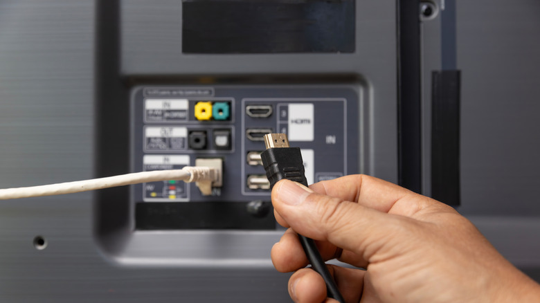 person holding HDMI cable next to back of a TV