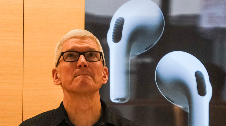 Apple CEO Tim Cook looking up with a big image of Apple AirPods in the background