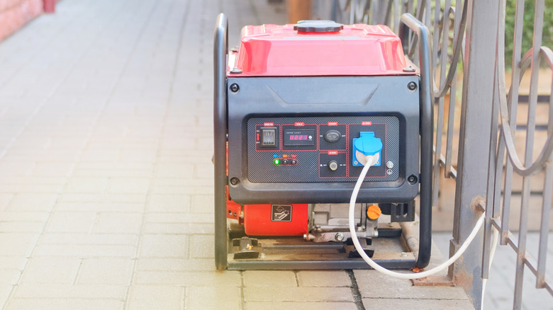 A red and black compact power generator next to a metal fence