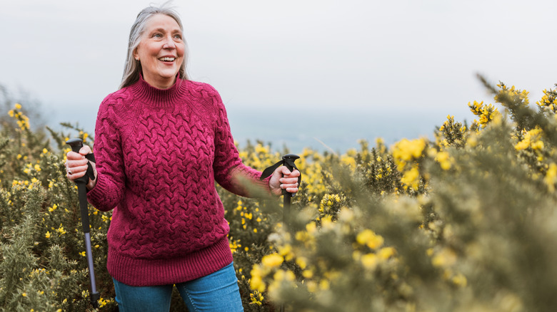 Senior woman hiking in nature, smiling in a pink sweater.