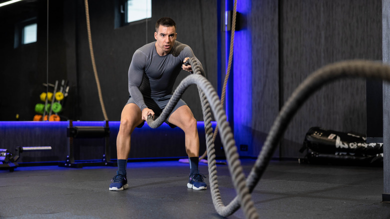 A strong man concentrating on enhancing his muscle tone through focused battle rope exercises within an innovative training space tailored for optimal workout performances.