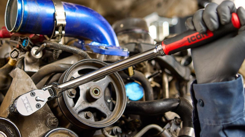 A gloved hand using a large Icon ratchet on a car engine.