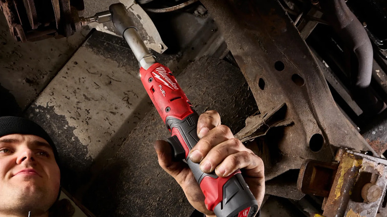 A man using a Milwaukee power ratchet on a car.