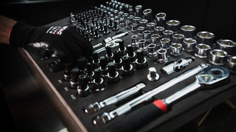 Gloved hand reaching for a Sonic Tools ratchet in a foam case