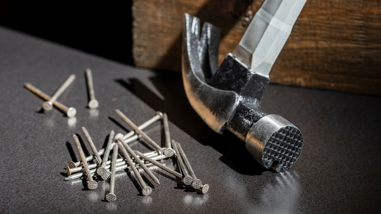 A claw hammer beside a pile of nails.