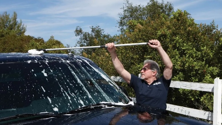 A man uses a telescoping car mop from harbor freight