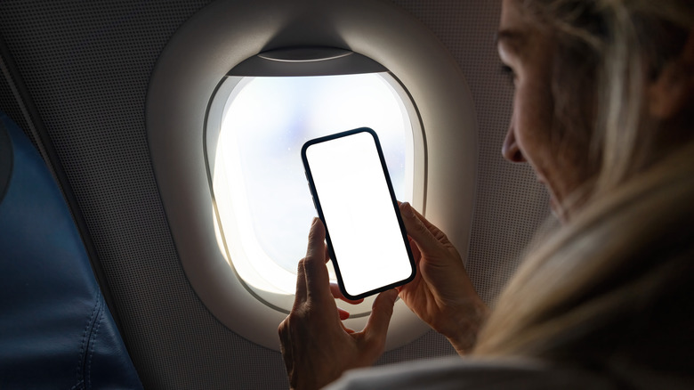 A woman on an airplane holding up a smartphone near the window