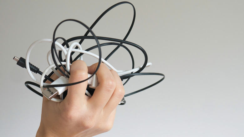 A close-up of a hand holding a tangle of white and black charging cables