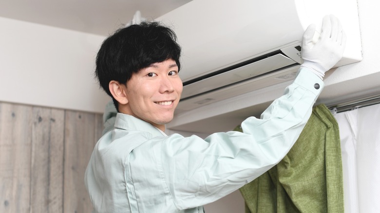 Man wearing white gloves smiling by AC unit