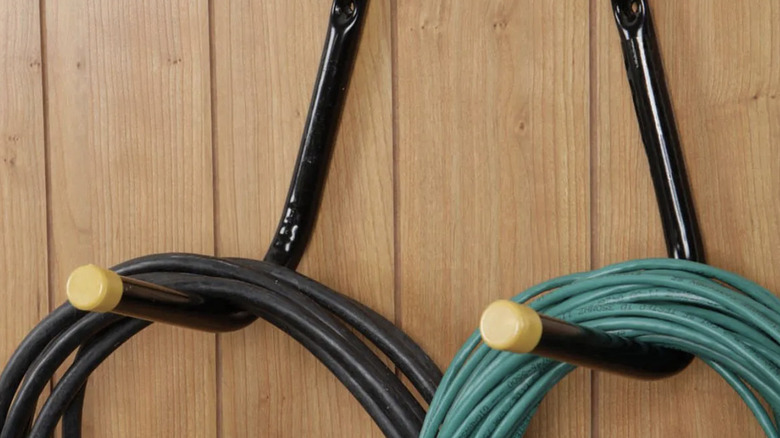 The Storehouse Hang-All V-shaped hook mounted on a wood wall and holding two hoses