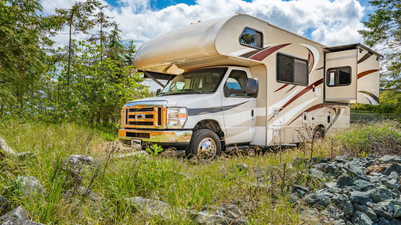 A cream color RV with red, black, and white accents parked in the grass.