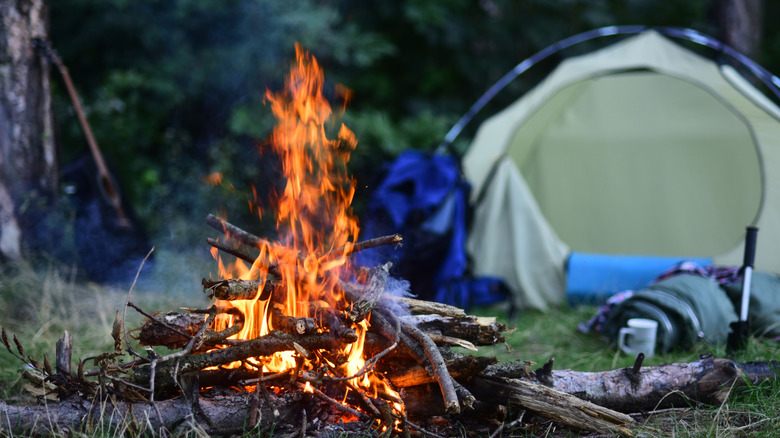 Camp fire with tent and camping equipment in the background