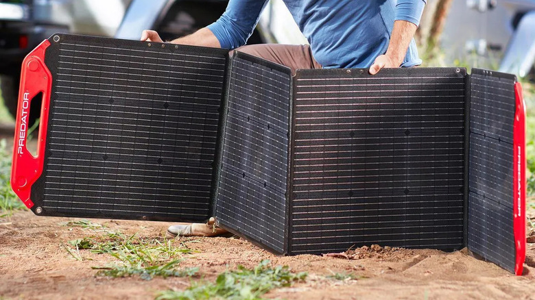 A person unfolds a red and black Predator solar panel