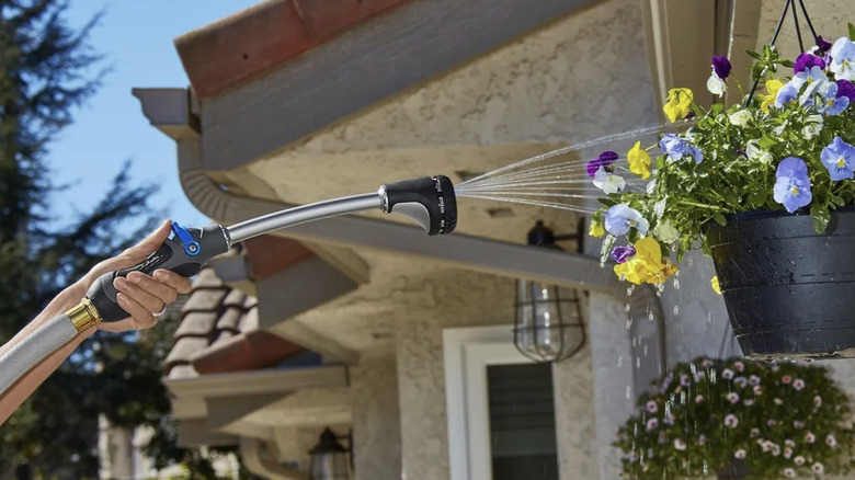 A hand holding up the Niagara multipattern watering wand to water a hanging flower basket outside a home