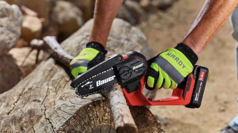 A man in yellow work gloves cutting through a thick branch with the Bauer cordless pruning saw