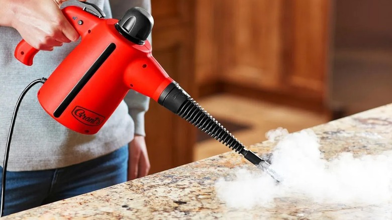 A person using a handheld steam cleaner on a counter.