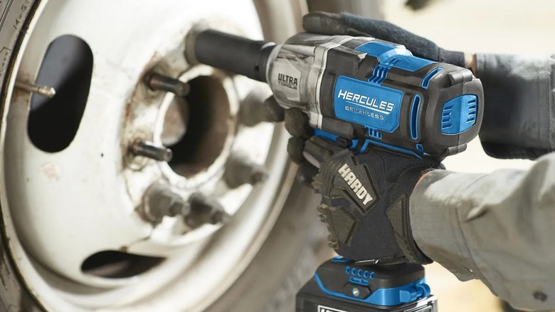 A worker using a Hercules impact wrench to remove lug nuts from a vehicle wheel.