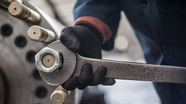 A mechanic using a large wrench to loosen an oversized nut