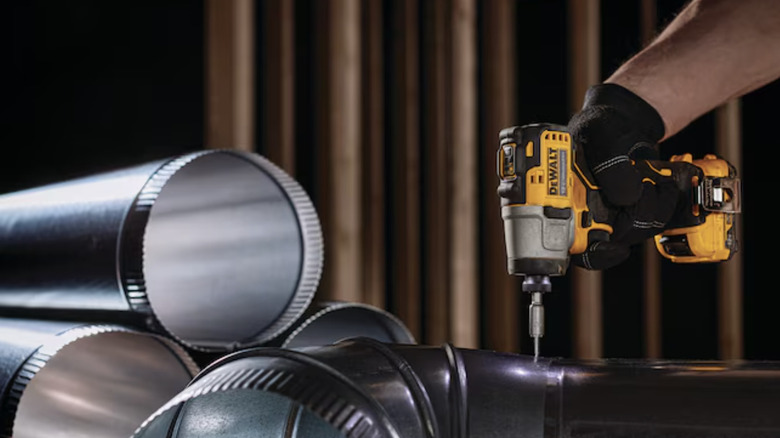 man using impact driver on pipes