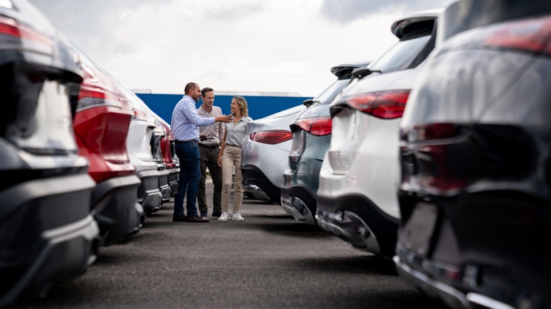 A used car dealer showing a couple around a used car lot.