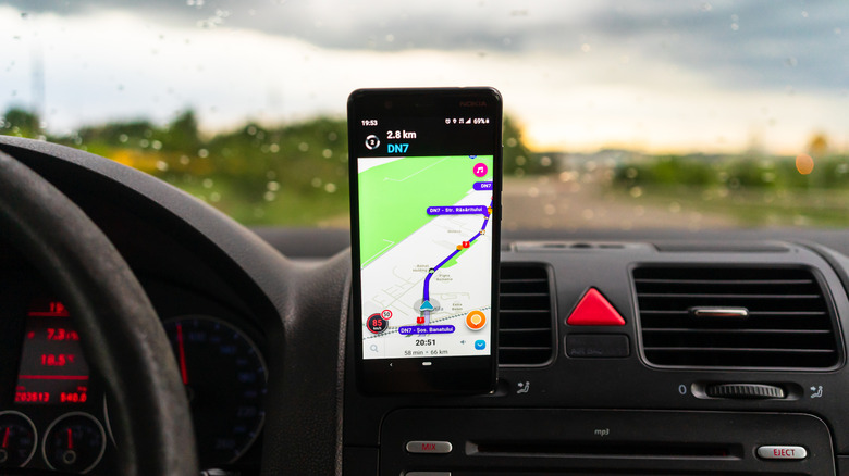 Waze app's navigation screen on a mobile phone on a car's dashboard.