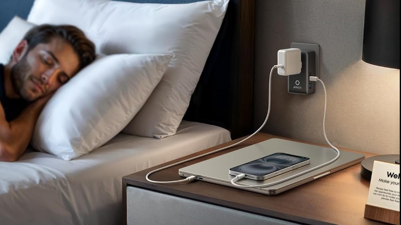 A man sleeping on bed next to a travel charger charging his gadgets