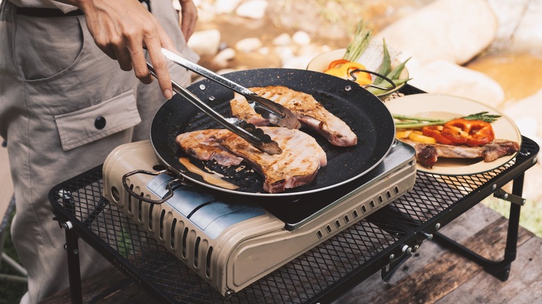 Person cooking pork chops on camping grill