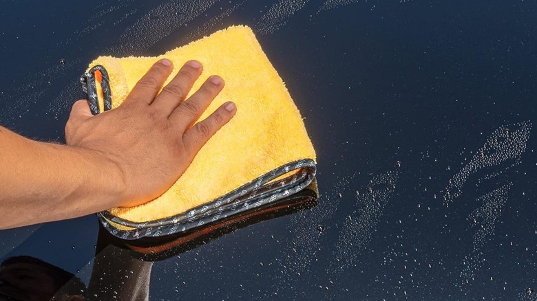 Close-up of a person using a Chemical Guys Miracle Dryer microfiber towel to dry a black vehicle