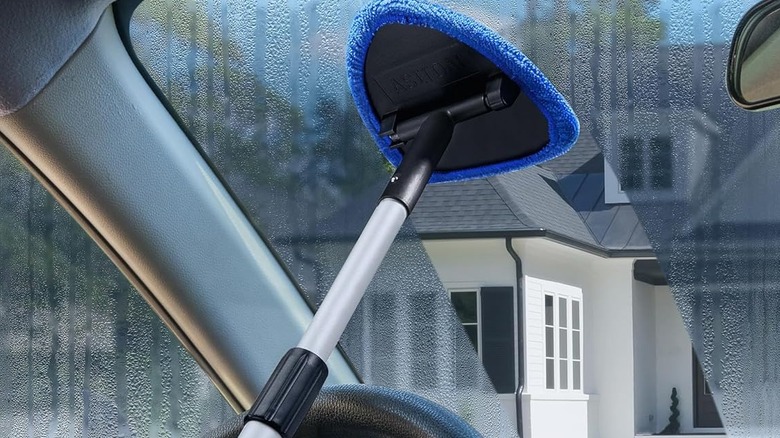 Someone using a windshield cleaner tool to clean the inside of their car's windshield