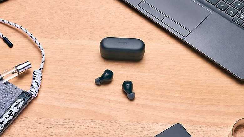 A pair of Sony WF-C510 wireless earbuds on a wooden desk next to a laptop computer