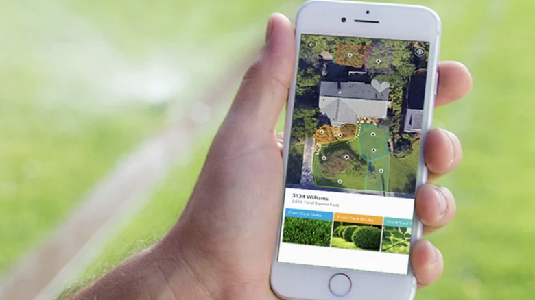 Close-up of a hand holding a smart phone displaying the Rachio Smart Sprinkler System app