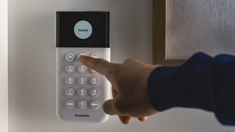 Close-up of a hand reaching for the key pad of a SimpliSafe security system