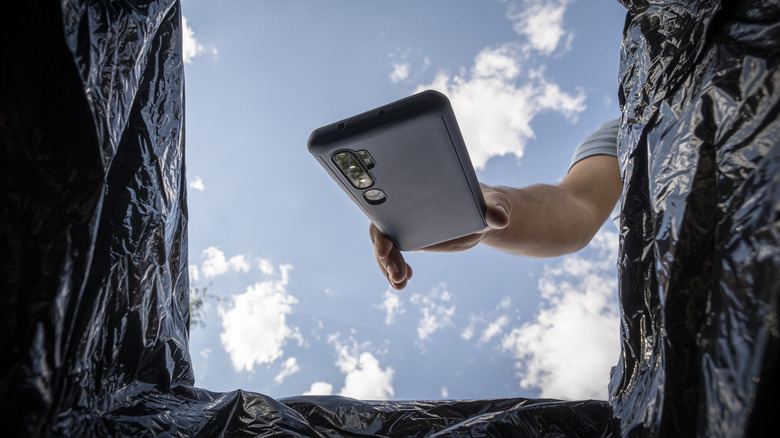 A man throwing a smartphone into a trash can, view from bottom of trash can