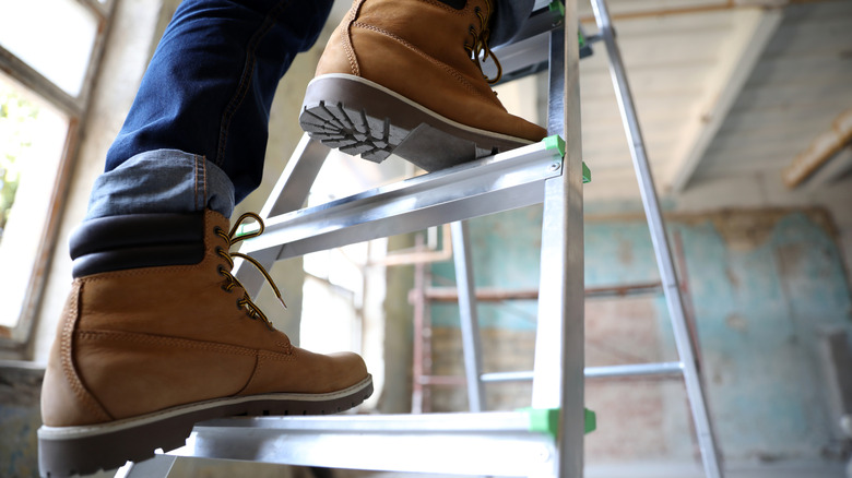 A close-up of a worker wearing boots ascending a ladder