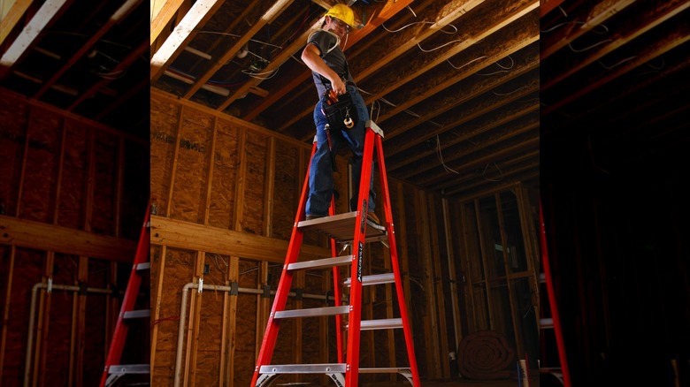 A worker on a construction site standing on the top rung of a Louisville Platform Ladder