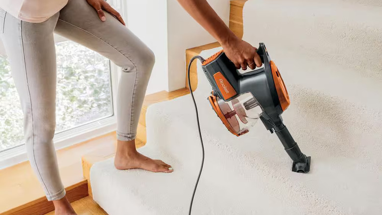 Person using a Shark Rocket stick vacuum on carpeted stairs