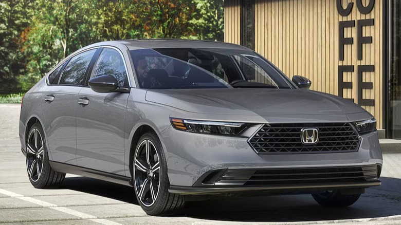 A 2026 sleek gray Honda Accord is parked outside a modern coffee shop with city buildings and trees in the background.