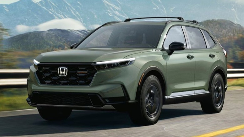 A 2026 green Honda CR-V cruises smoothly along a winding mountain highway surrounded by colorful autumn scenery.
