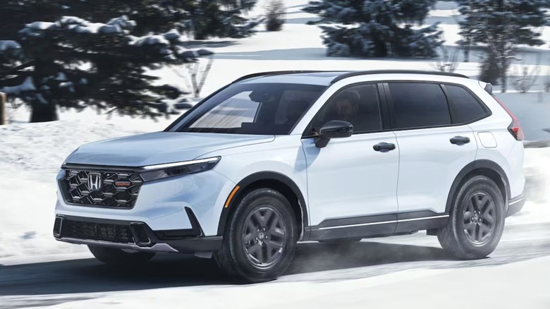A 2026 white Honda CR-V drives confidently through a snowy landscape, sending light snow spraying behind its tires.
