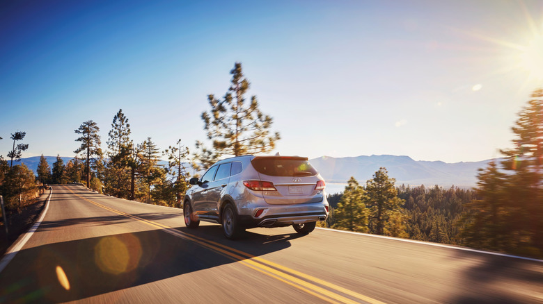 2018 Hyundai Santa Fe driving against sunny forested background, rear-left view