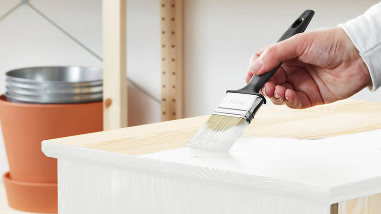 A person painting a wood box a white color