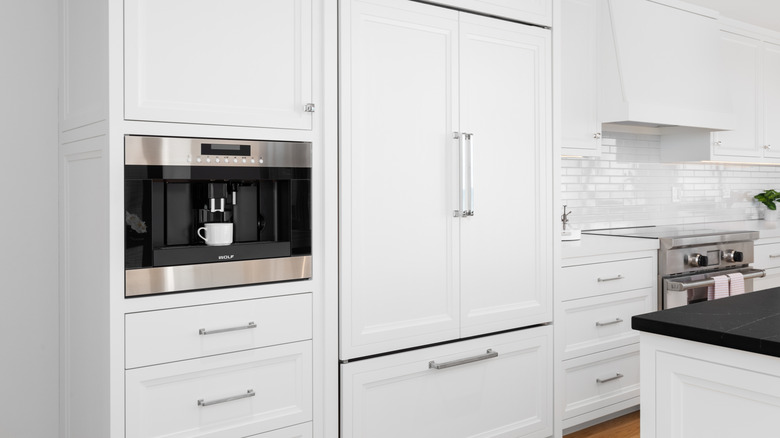 A white, luxurious kitchen with Sub-Zero refrigerator and built-in Wolf coffee maker.