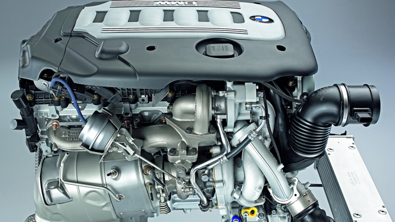 A silver BMW N54 engine from the 2006 BMW 335i sedan with its engine cover on a white backdrop.